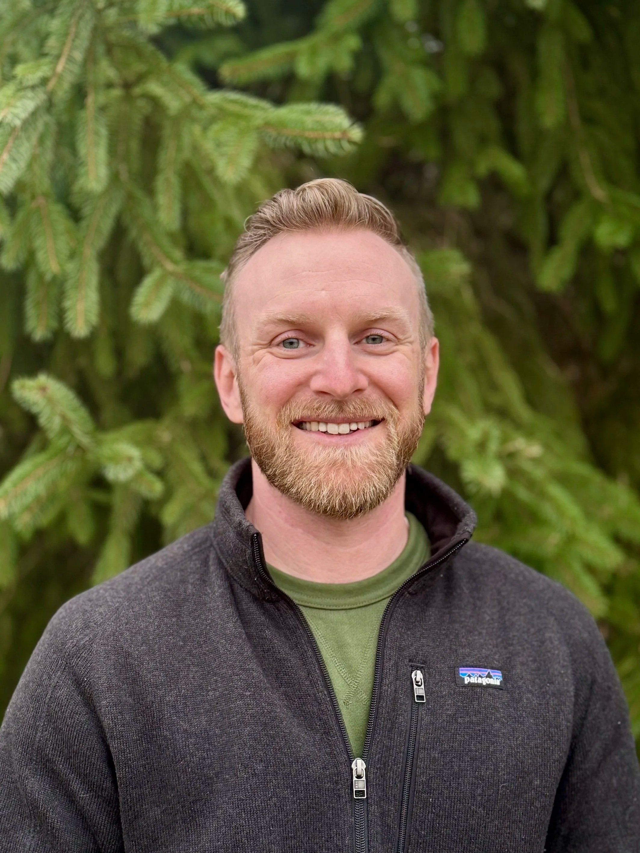 Owner Stewart Cory with long hair outdoors, wearing a necklace.