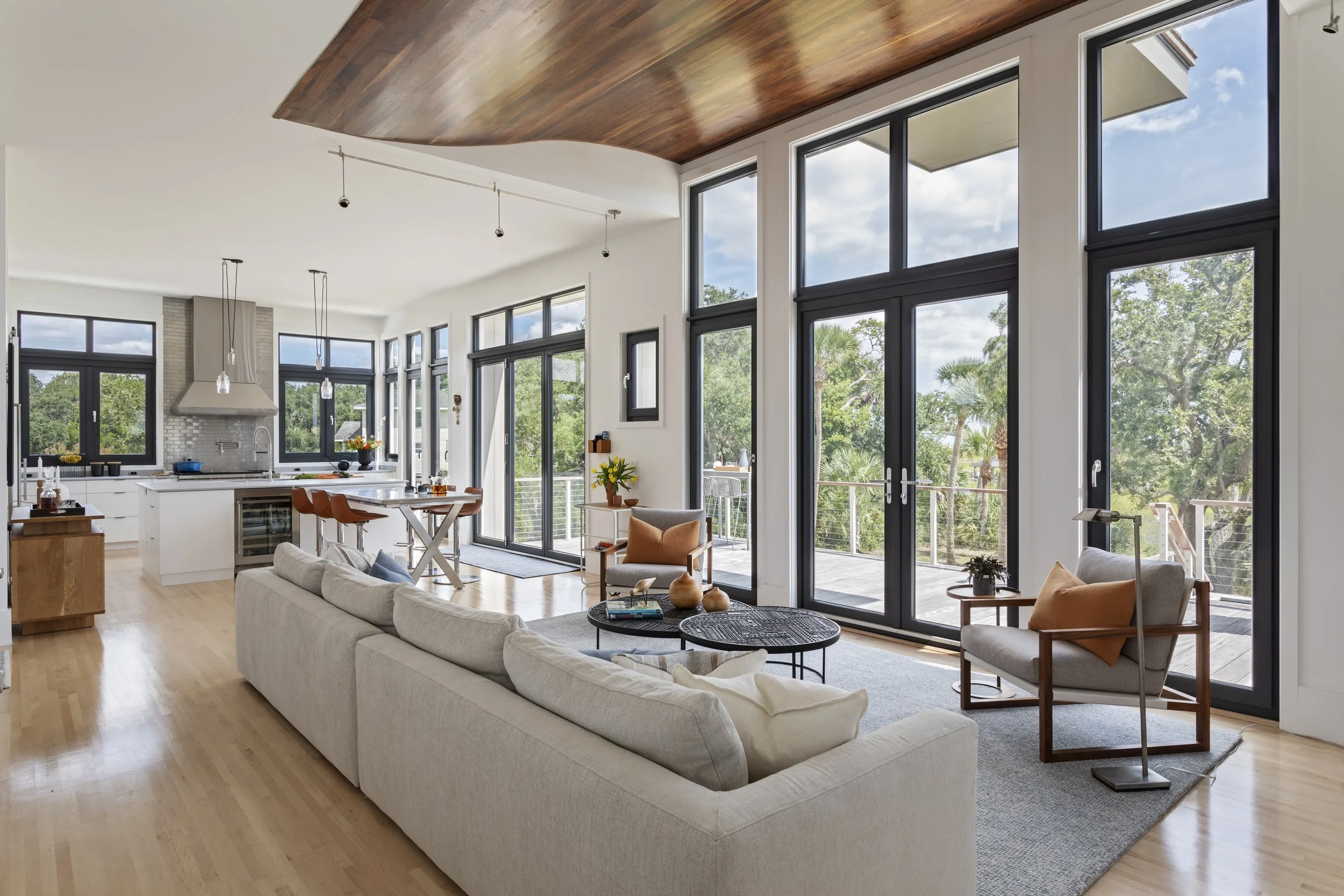 Spacious living room with large windows, white sofa, armchairs, and a view of trees outside.