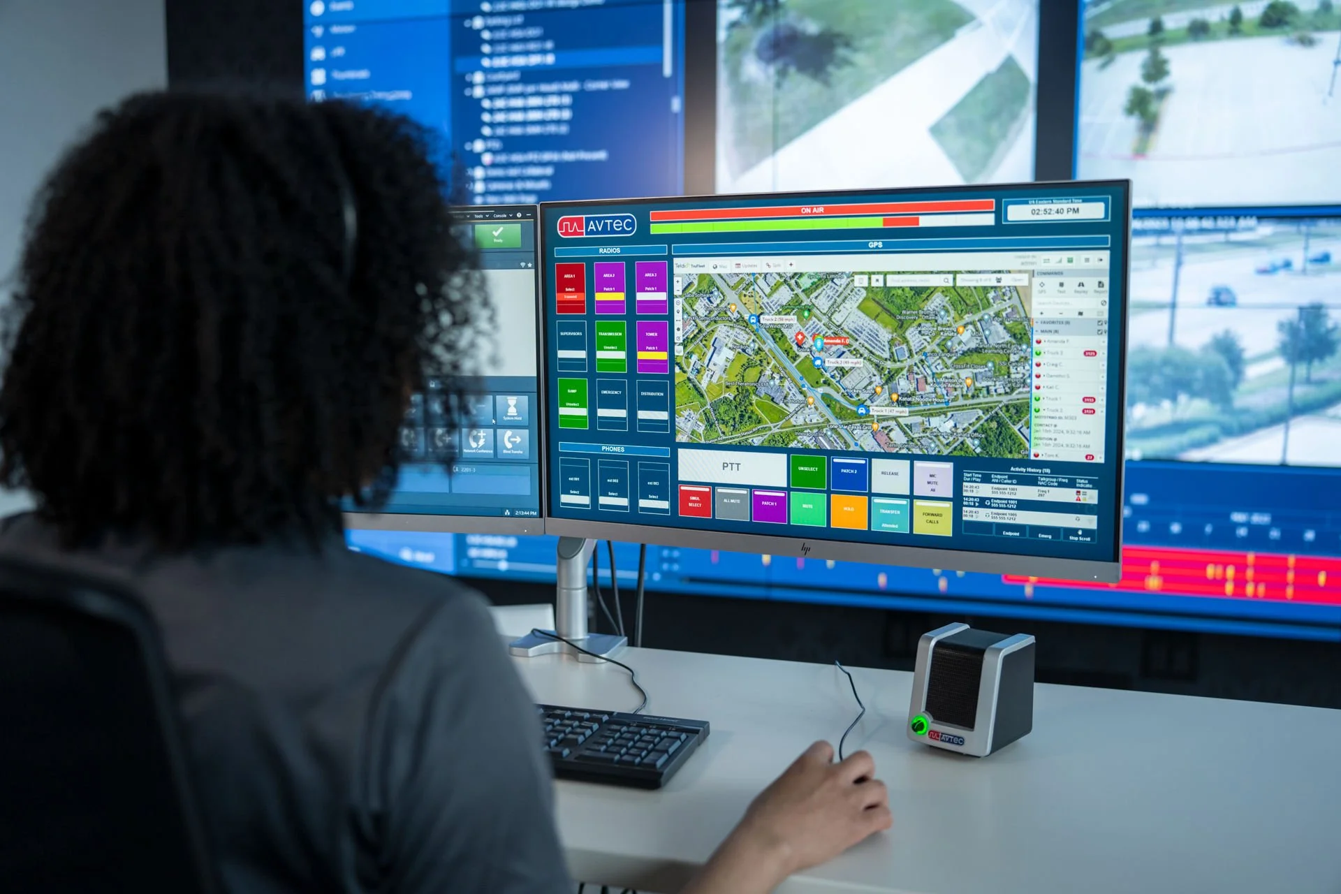 A person working at a control desk with multiple monitors displaying maps and communication interfaces, likely in a traffic or security monitoring center.
