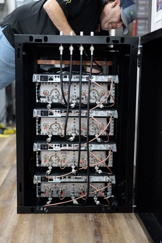 Man working on an open server rack with electronic equipment and cables inside.