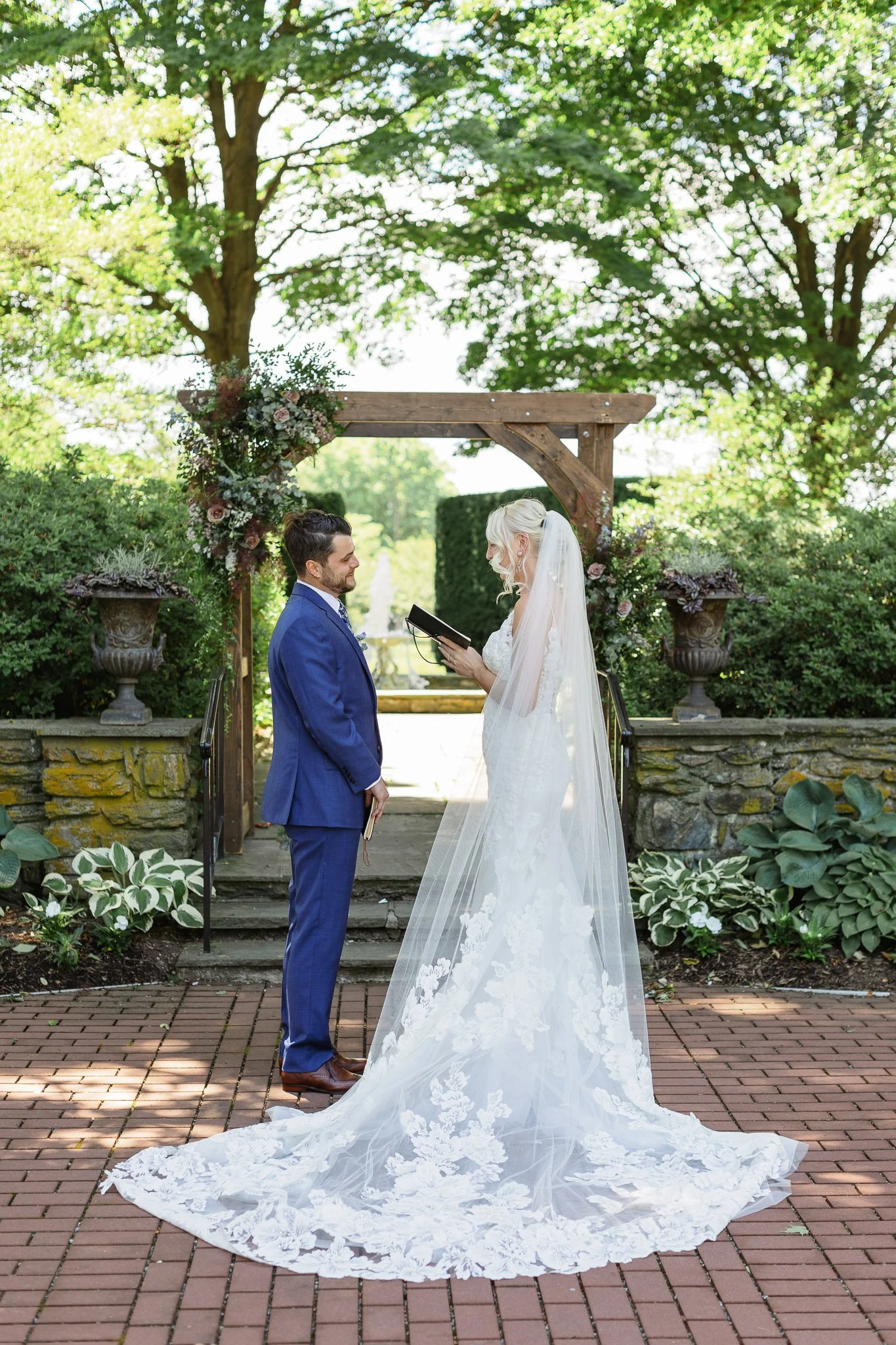 A bride in a lacy white dress and a groom in a blue suit sharing a private moment in The Gardens at Drumore Estate.