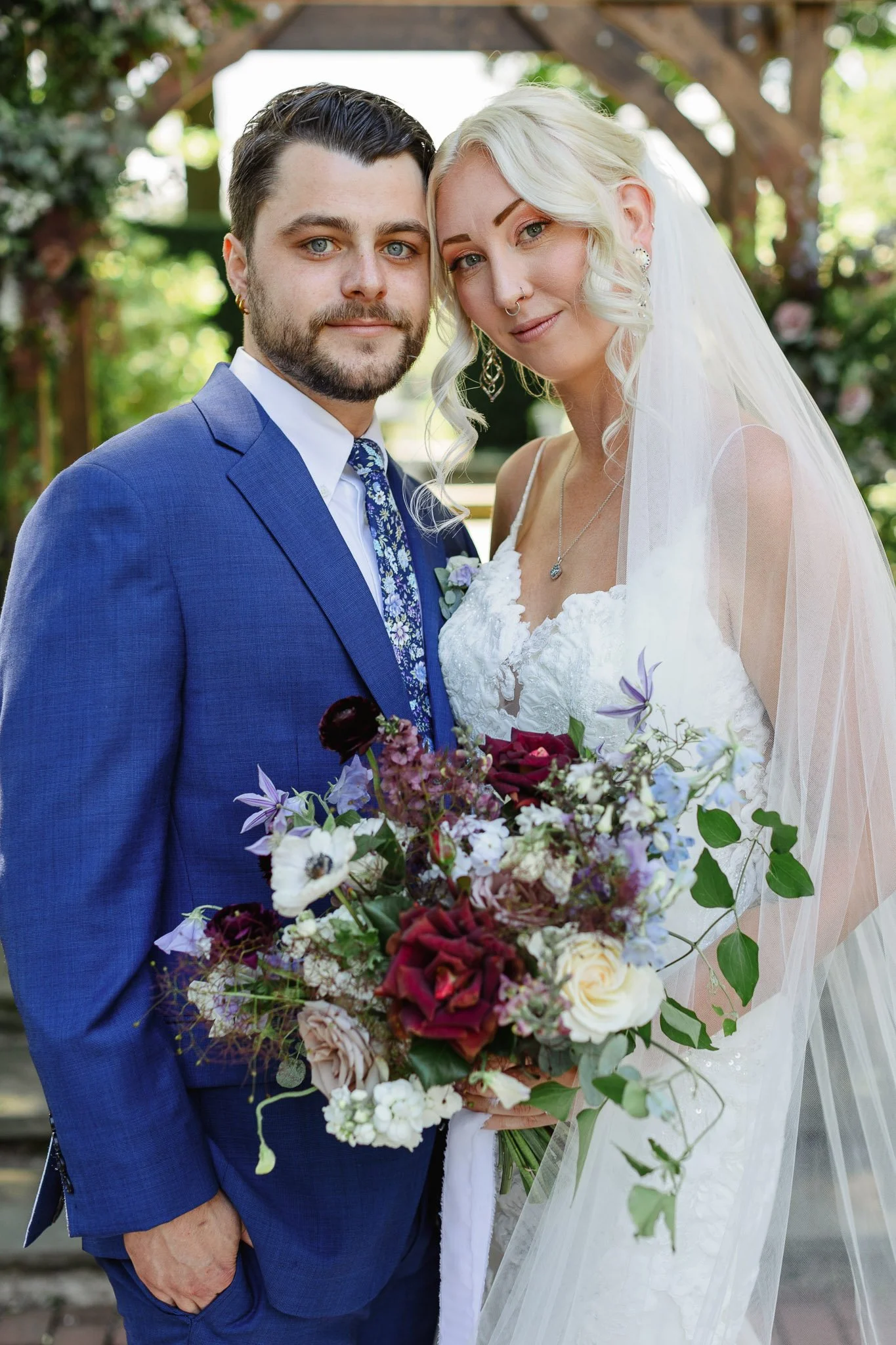 A beautifully framed wedding photo highlighting the textures of a lace dress and a blue suit in a garden setting.