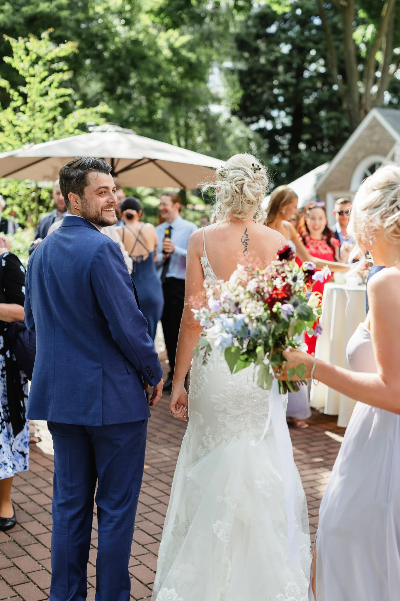A candid wedding photo of the bride and groom laughing with guests during a sun-drenched cocktail hour in The Gardens.