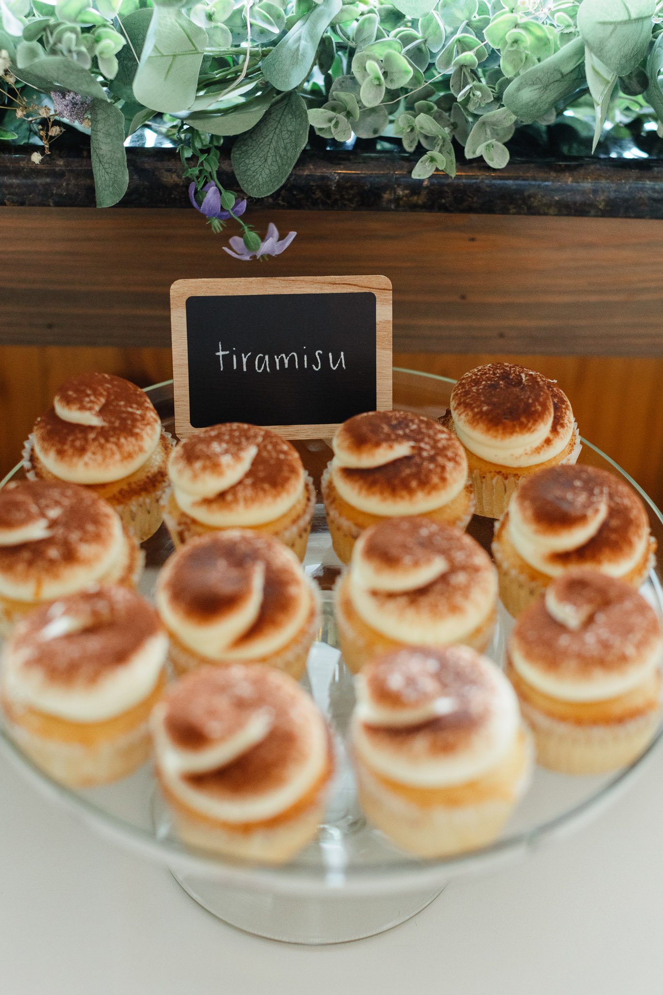 A delicious close-up of tiramisu cupcakes with cocoa dusting and cream frosting, displayed on a dessert table at the wedding reception.