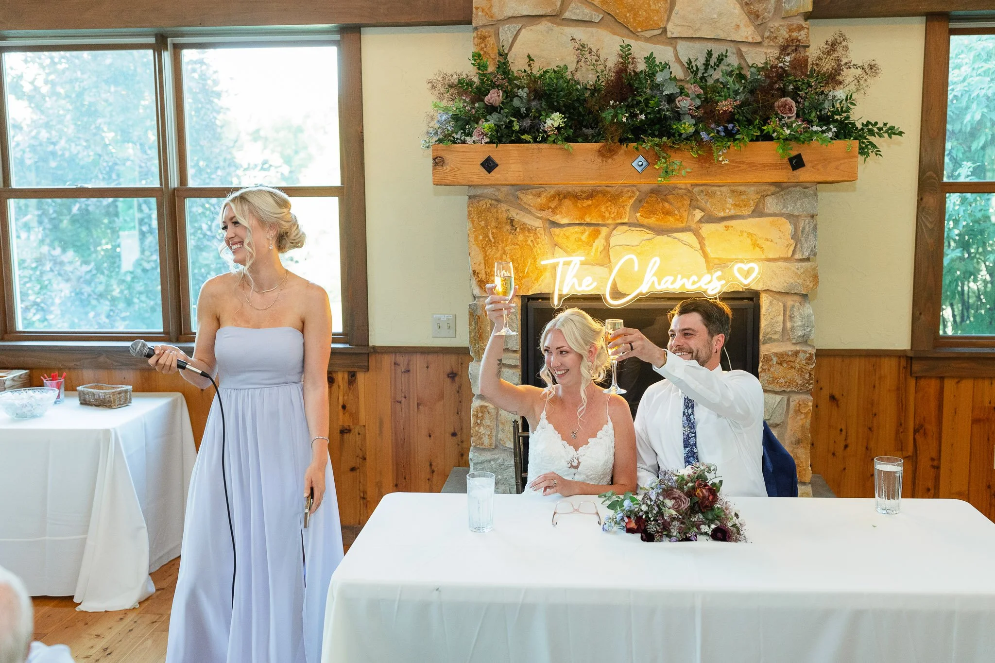 A candid wedding photo of the bride and groom at their sweetheart table, reacting with laughter to the maid of honorspeech.