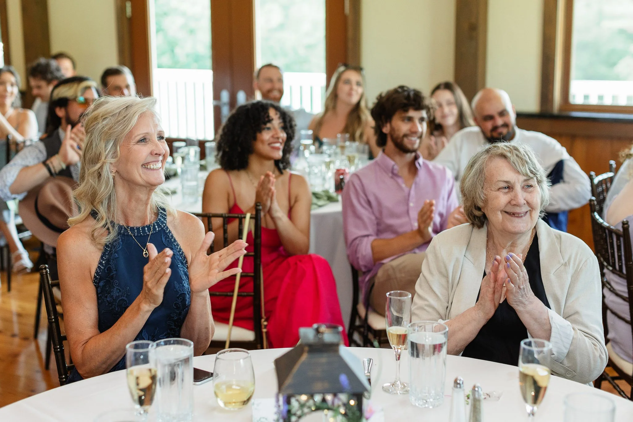 A wide shot of the reception guests laughing and applauding during the best man's speech in the Drumore Estate ballroom.