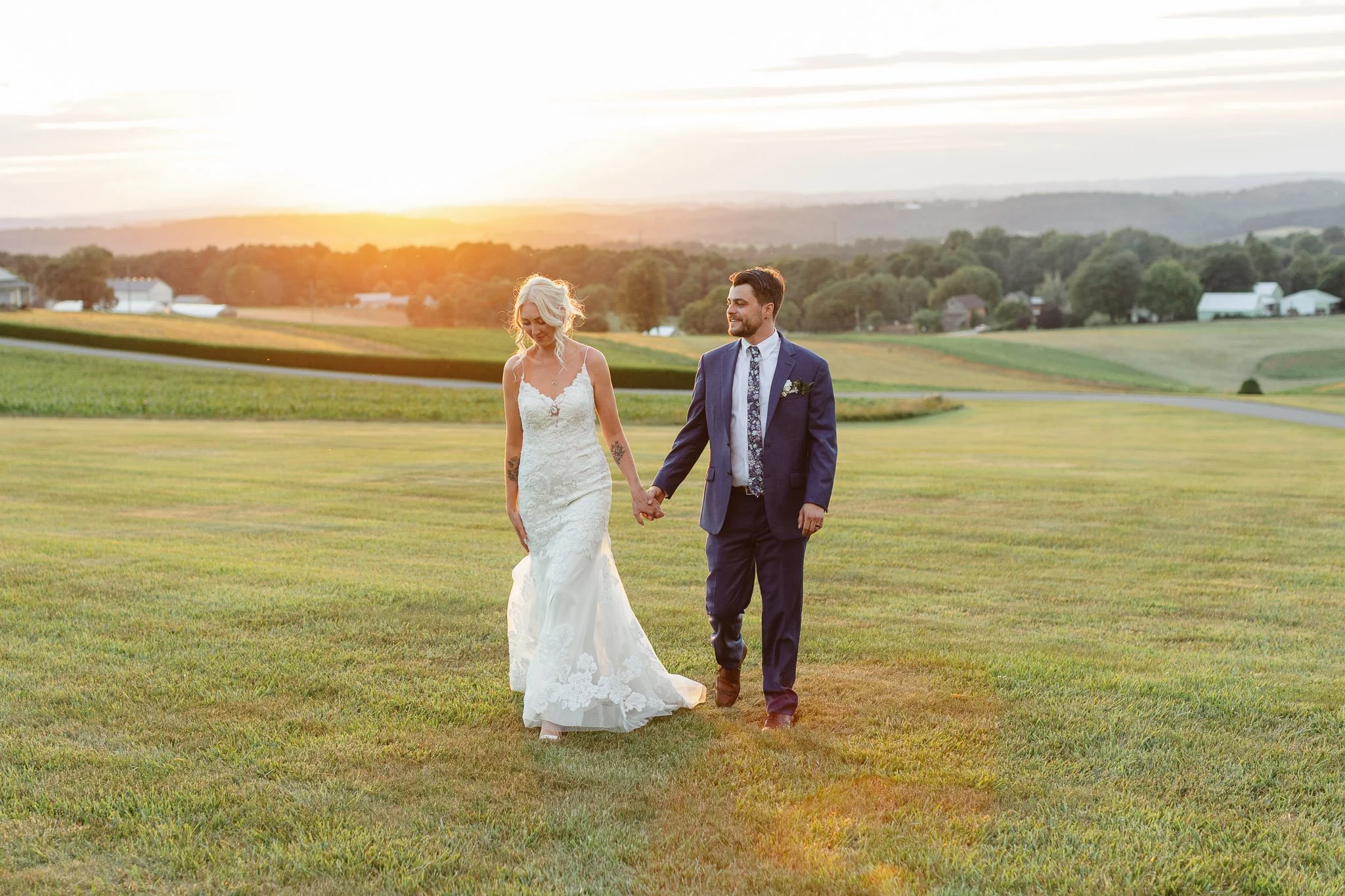 The couple standing in an open field in Pequea, with the "golden hour" light illuminating the bride's white lace dress.