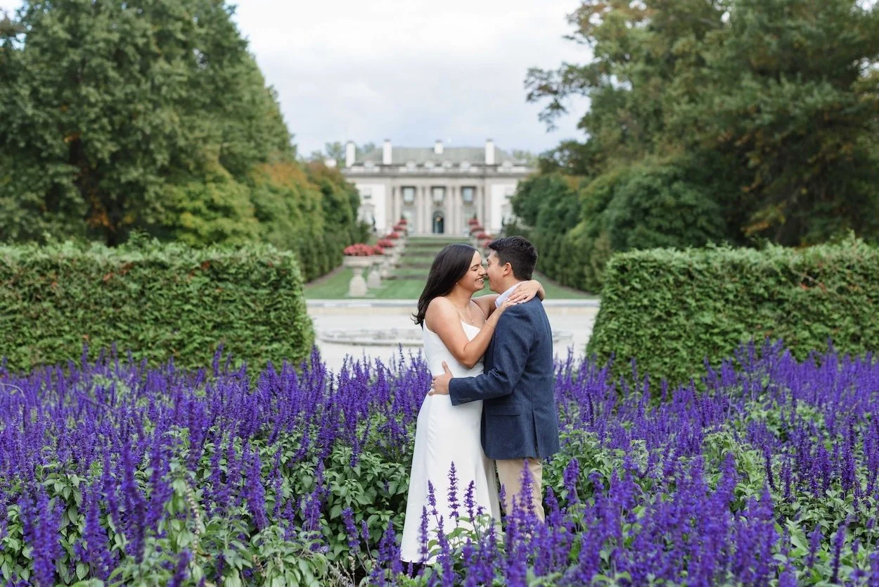 A couple's engagement session in a field of beautiful purple flowers in front of a gorgeous mansion