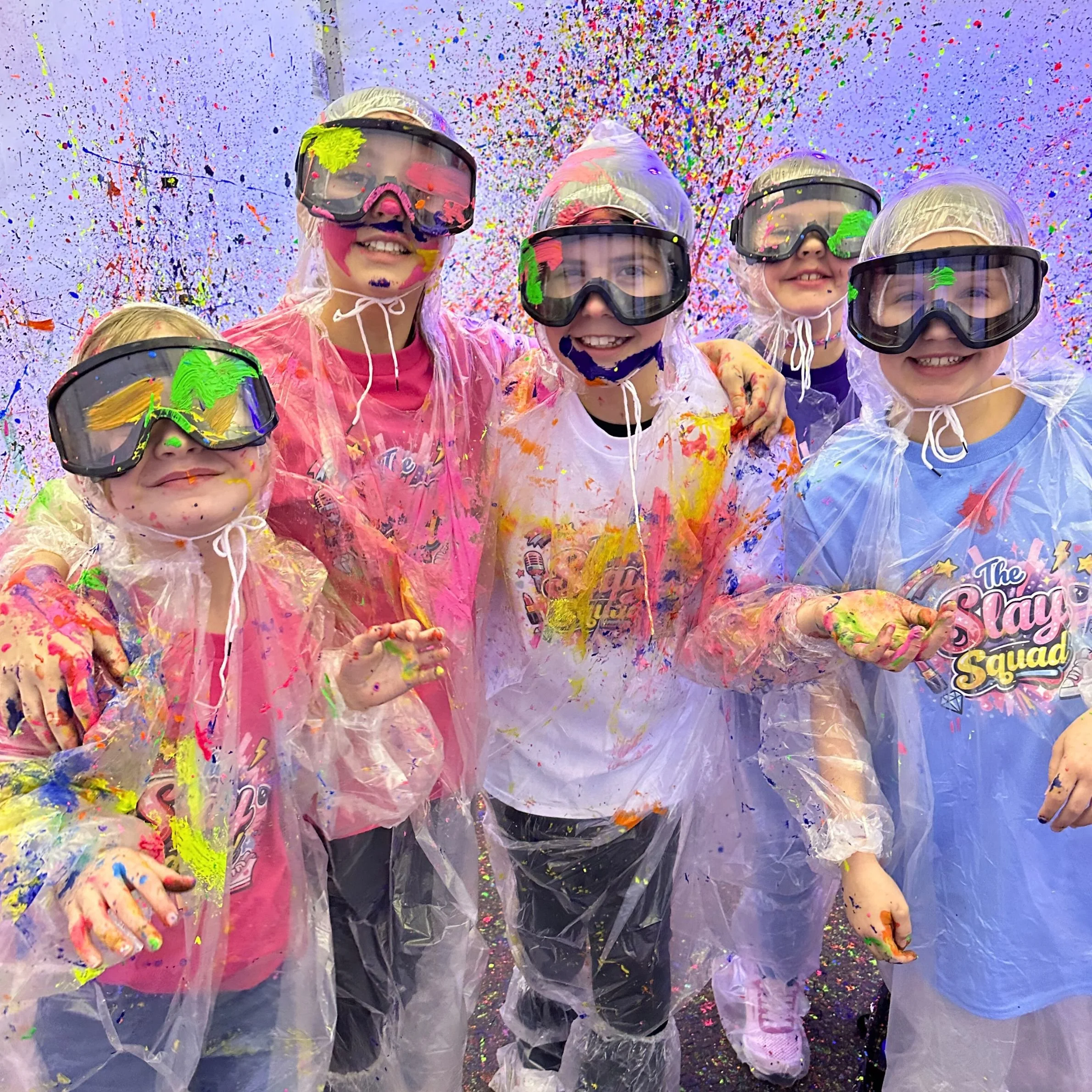 Kids wearing goggles and ponchos during a fun splatter paint birthday party experience at Crafty Beings DIY studio in Seekonk Massachusetts.