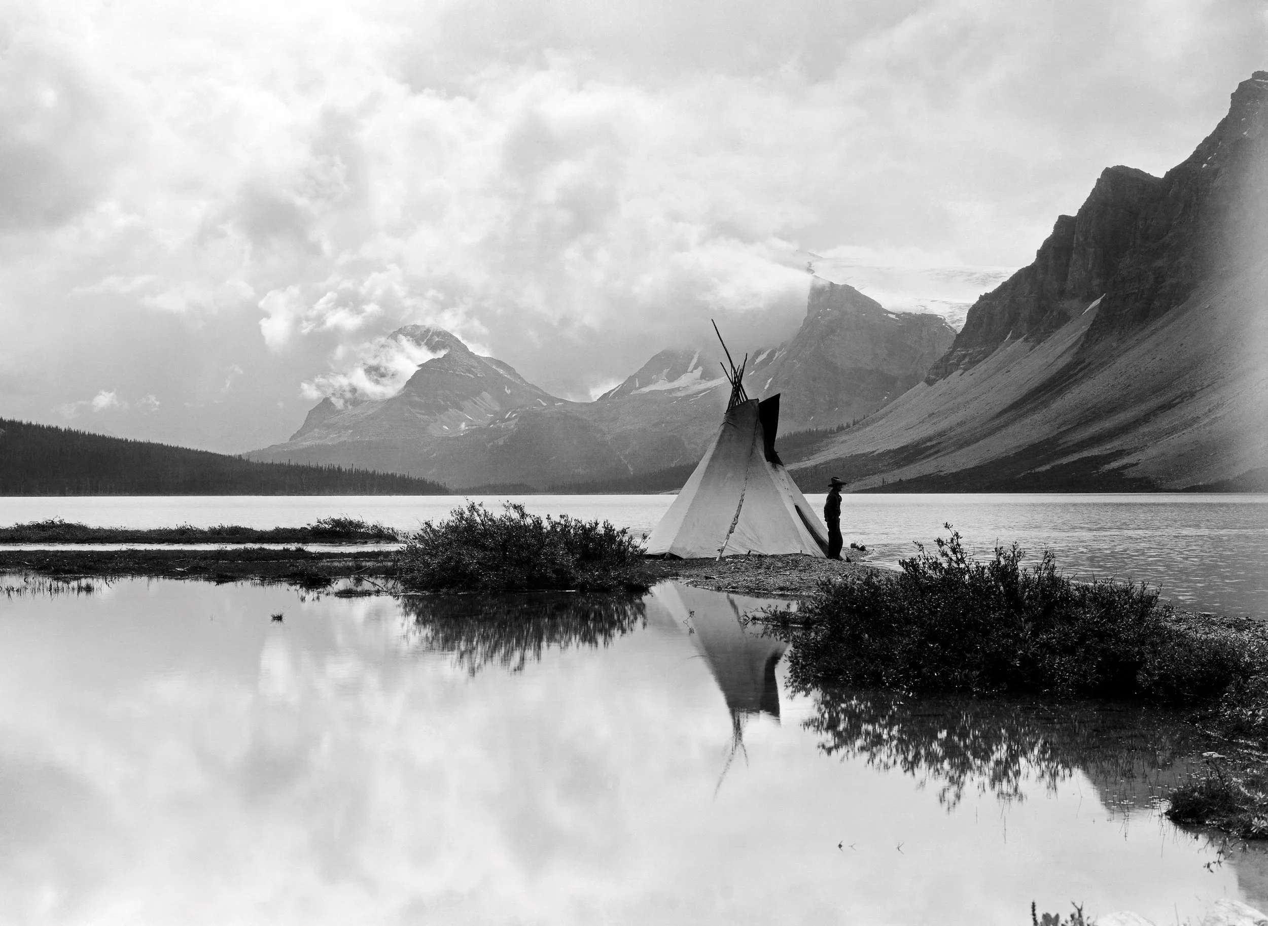 Byron Harmon, Teepee at Bow Lake, with Rob Baptie || The expedition route follows Bow River to its headwater at Bow Glacier and Bow Lake. The teepee in this photograph is erected in marshy conditions on the lake edge, a perfect view of what will beco