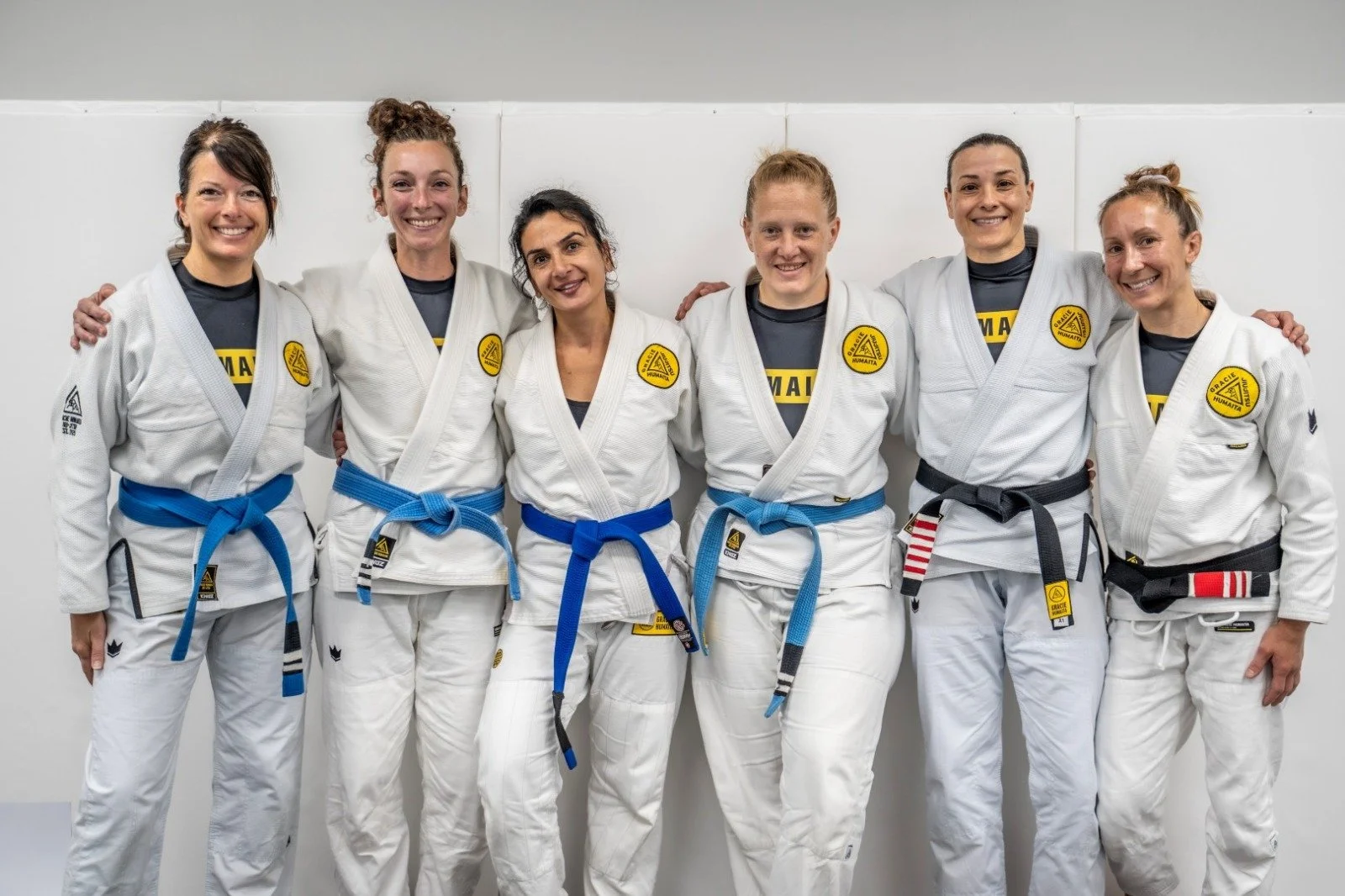 Group of women in Brazilian Jiu-Jitsu uniforms standing together, smiling, with arms around each other, in the Forged martial arts gym located in Ozark, Nixa, Springfield MO.