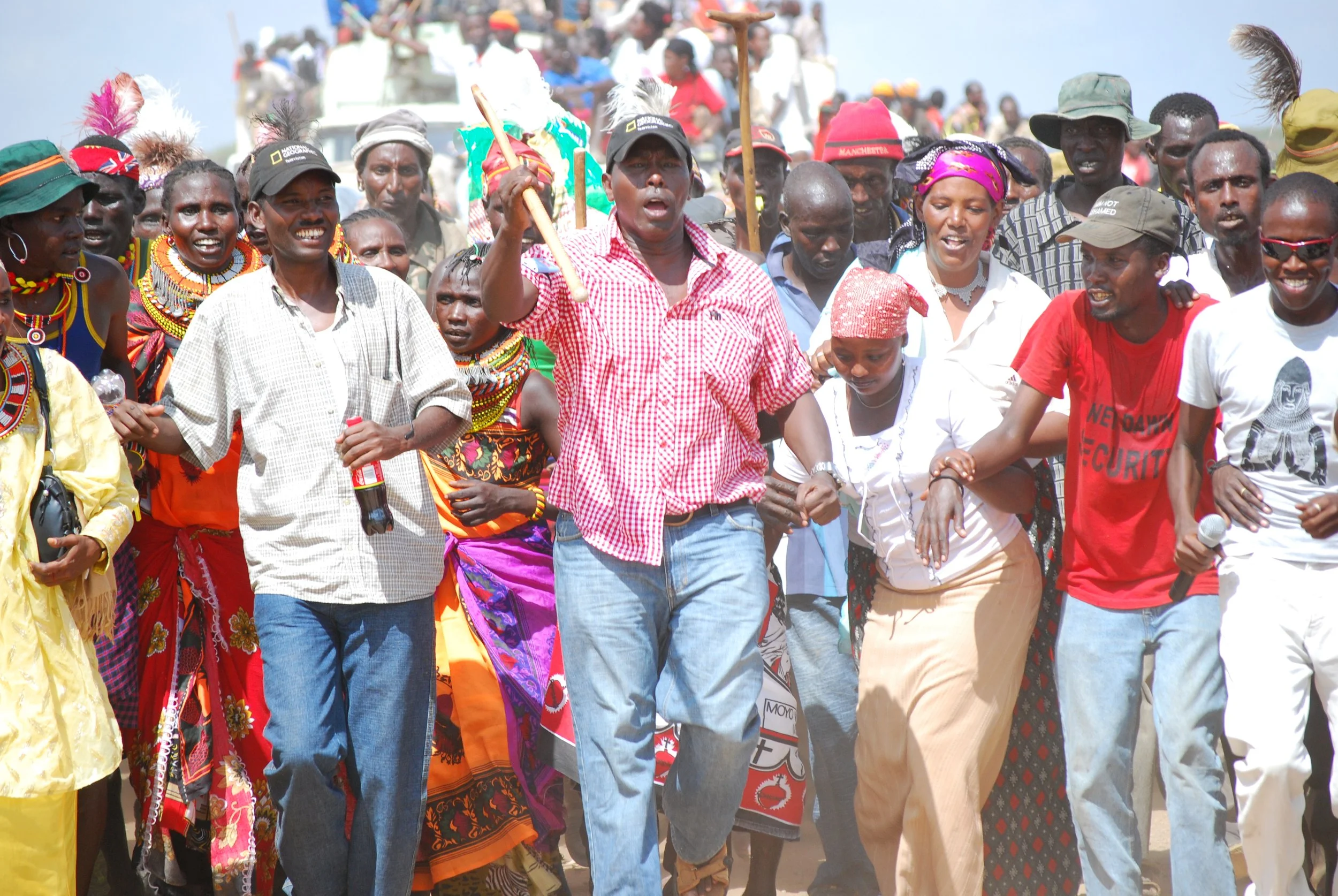 A group of people dancing and celebrating outdoors at part of a political rally, dressed in colorful traditional and casual clothing.
