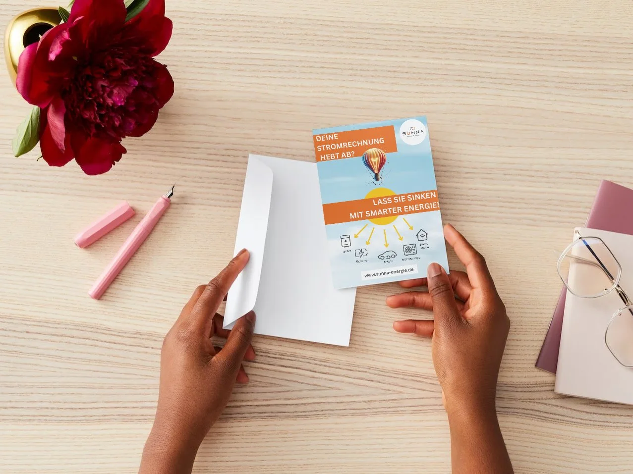 Person hält einen Flyer mit Energiespar-Werbung; daneben ein Umschlag, Füllfederhalter, Brille und rote Blume auf einem Holztisch.
