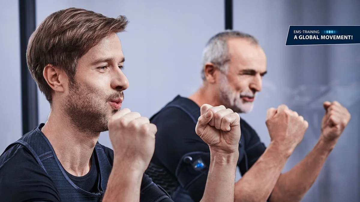 Zwei Männer bei EMS-Training, die ihre Fäuste in die Luft stemmen, im Fitnessstudio, mit Text "EMS-Training - A Global Movement!"