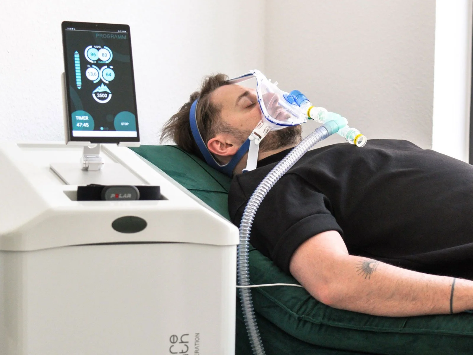 Mann liegt auf einer Liege und atmet abwechslungsweise viel und wenig Sauerstoff ein. Er macht ein Höhentraining um seinen Stoffwechsel zu optimieren.