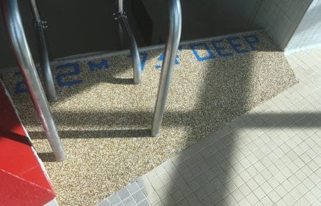 Rubberstone swimming pool edge with depth markings in meters and feet, metal ladder, tiled floor.