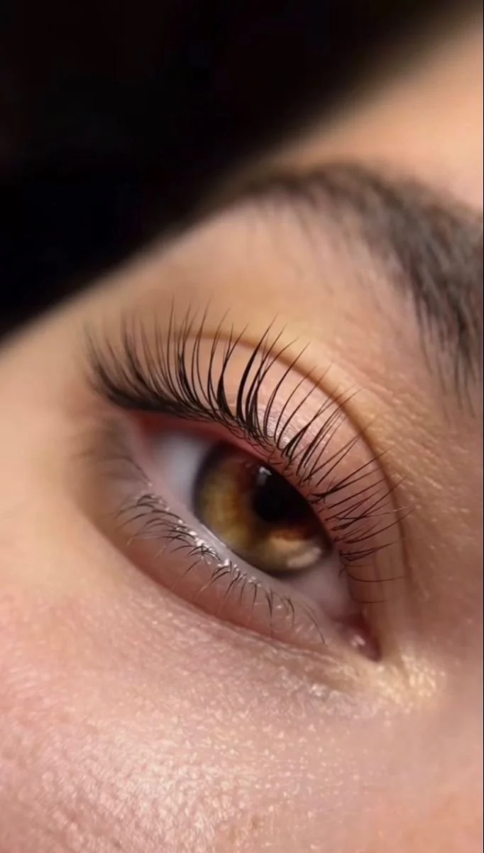 Nahaufnahme eines menschlichen Auges mit brauner Iris und langen Wimpern.