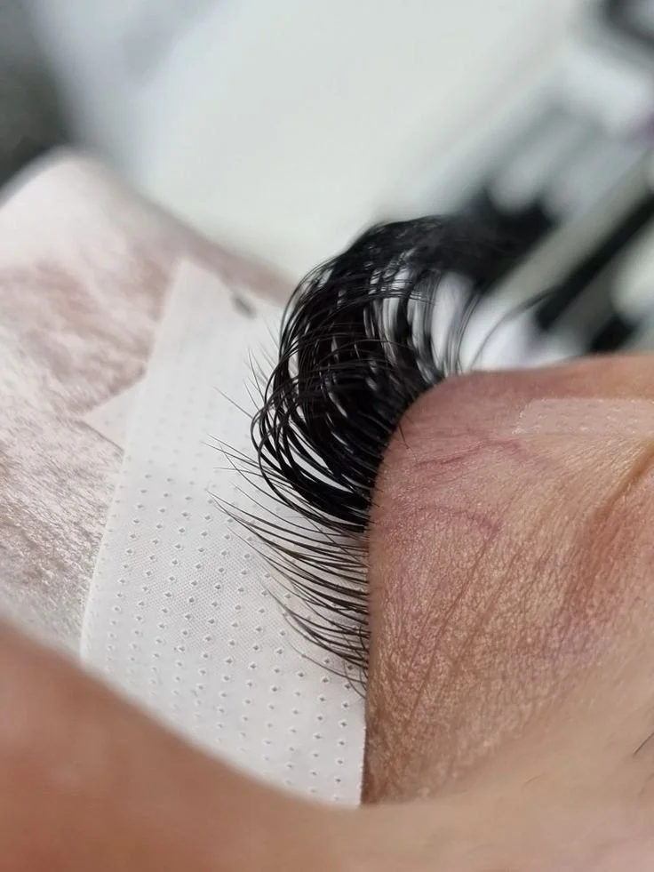 Nahaufnahme von einem Auge mit schwarzen Wimpern, die auf einem weißen, gepunkteten Papier ruhen.