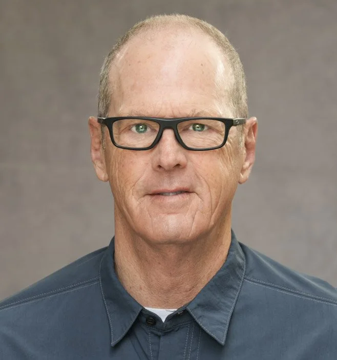 Man with glasses and short hair in a blue shirt, neutral background.