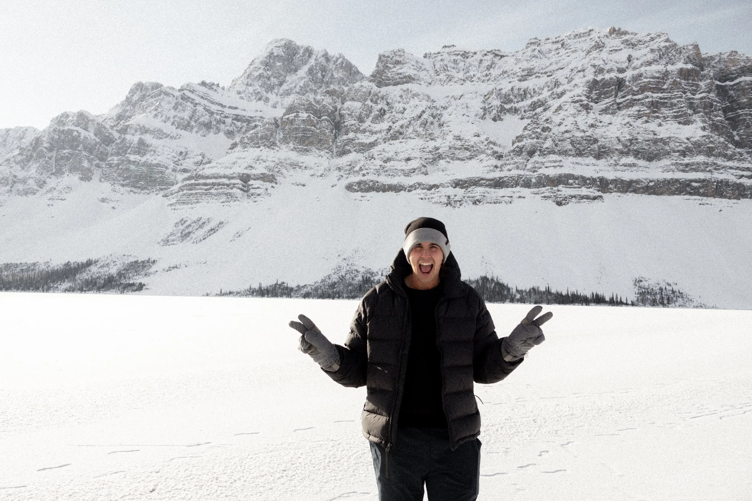 Person in winter clothing standing on snow-covered land with mountainous landscape in the background.
