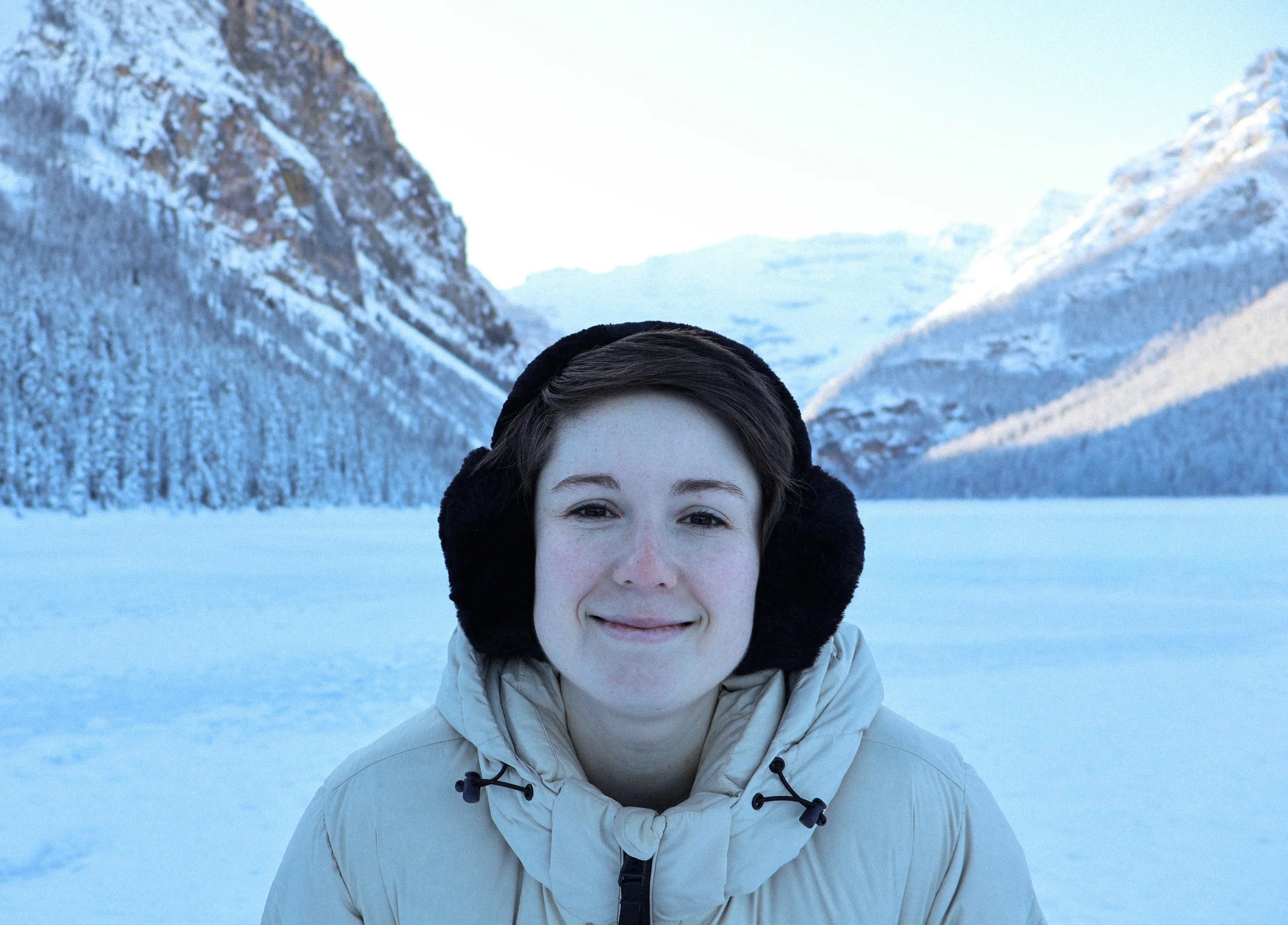 Young woman smiling in winter jacket and ear muffs in snowy mountain landscape