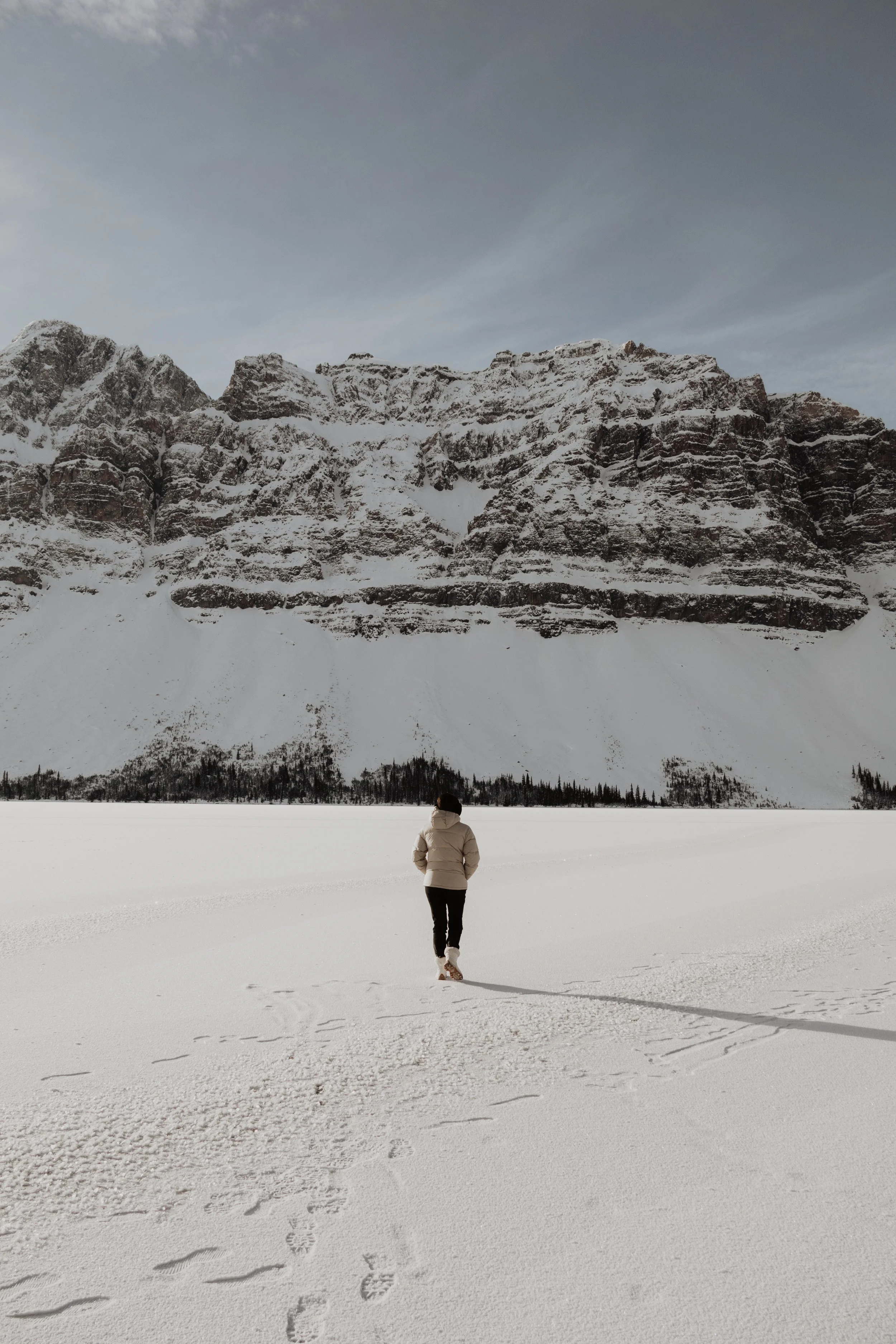 A person walking in a snowy landscape beneath a mountain range.