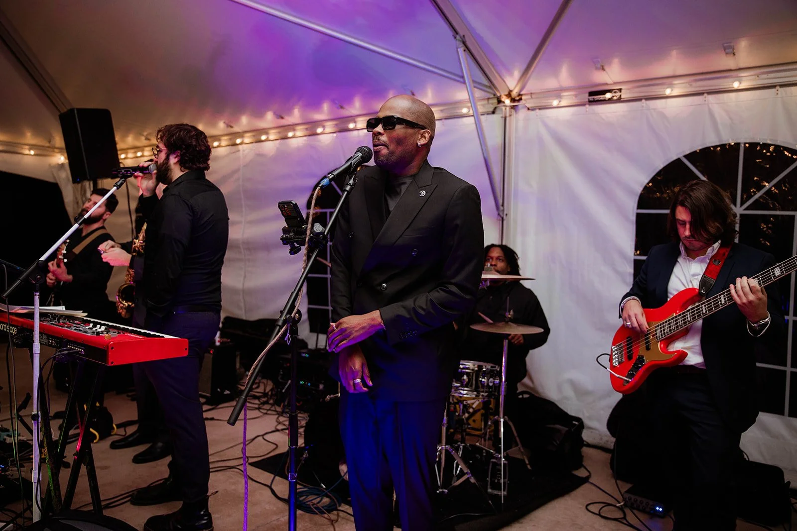 Live band performs during a wedding reception under a tent with glowing string lights, creating an energetic and festive atmosphere — planned by Charlotte Wedding Planner.