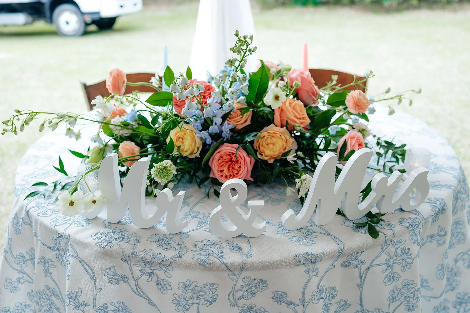 Sweetheart table decorated with peach and pink florals and a “Mr & Mrs” sign on a blue-patterned tablecloth — coordinated by Charlotte Wedding Coordinator.