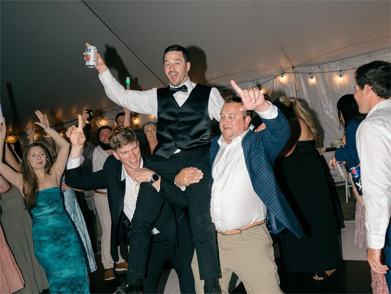 Groom being lifted by friends on the dance floor at the wedding reception.