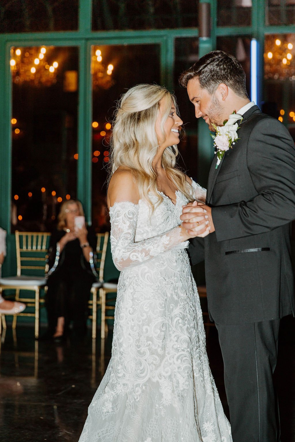 Bride and groom share their first dance surrounded by loved ones, glowing chandeliers, and soft floral décor — planned by Charlotte Wedding Planner at The Little Chapel at Haven Ridge.