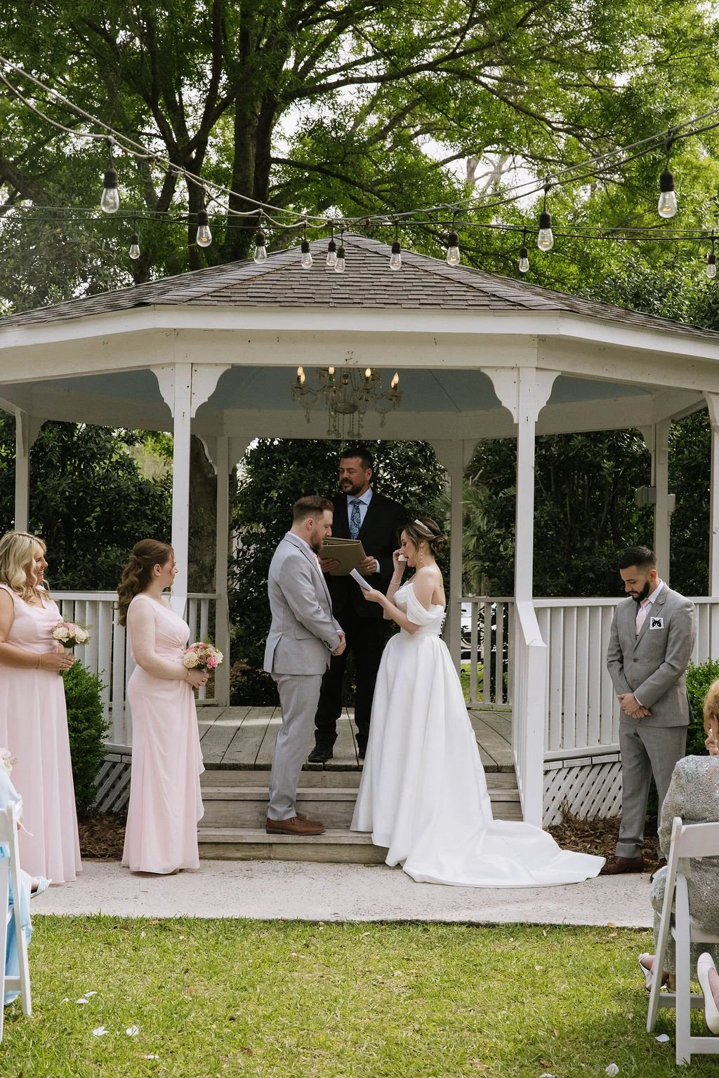 Bride reads heartfelt vows to her groom during an emotional gazebo ceremony with soft pink florals and elegant décor — planned by Charlotte Wedding Planner.