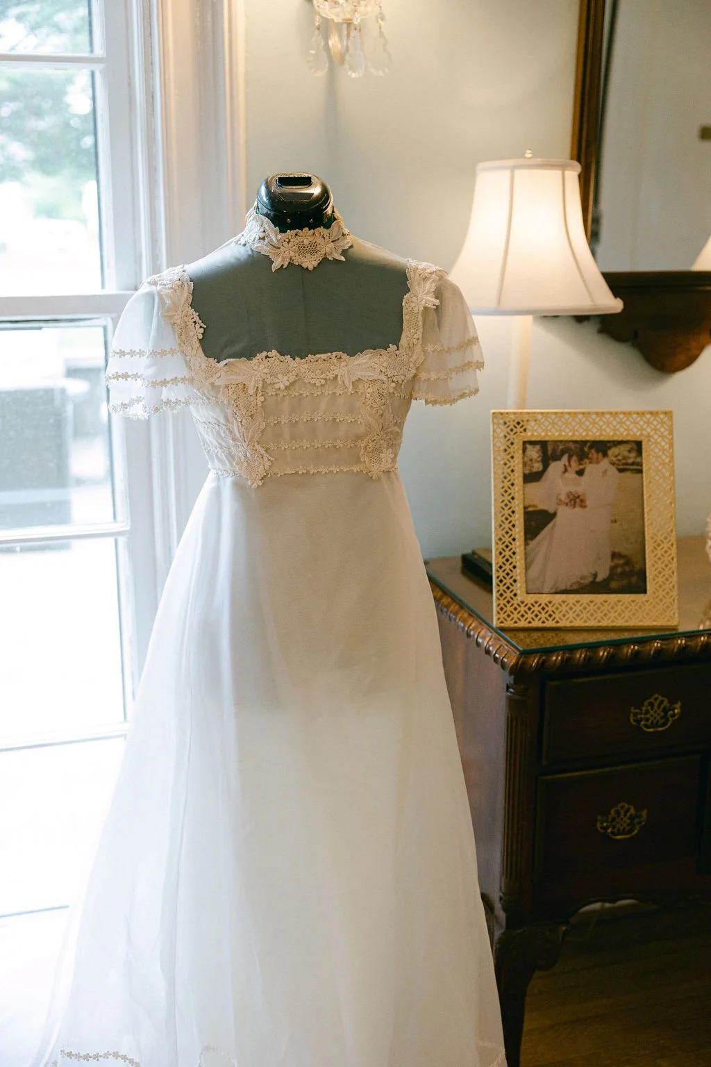 A vintage wedding dress displayed beside a framed photo of a past bride, representing a meaningful ‘something old’ heirloom detail for a wedding day.