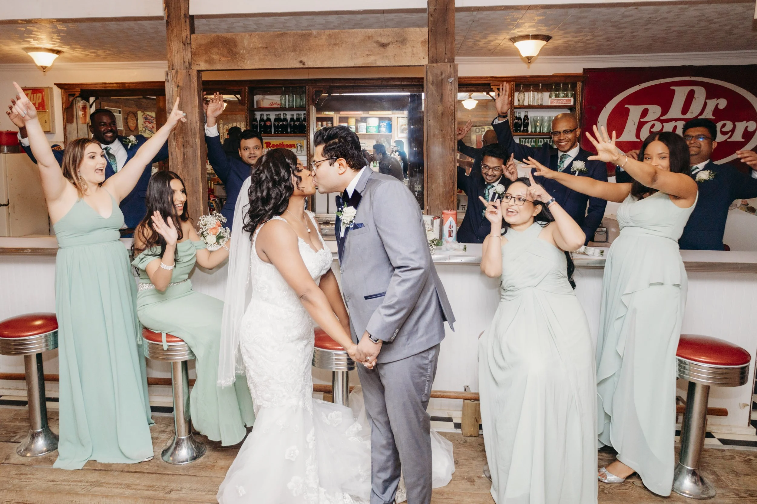 Couple sharing a kiss while their bridal party cheers in the background.