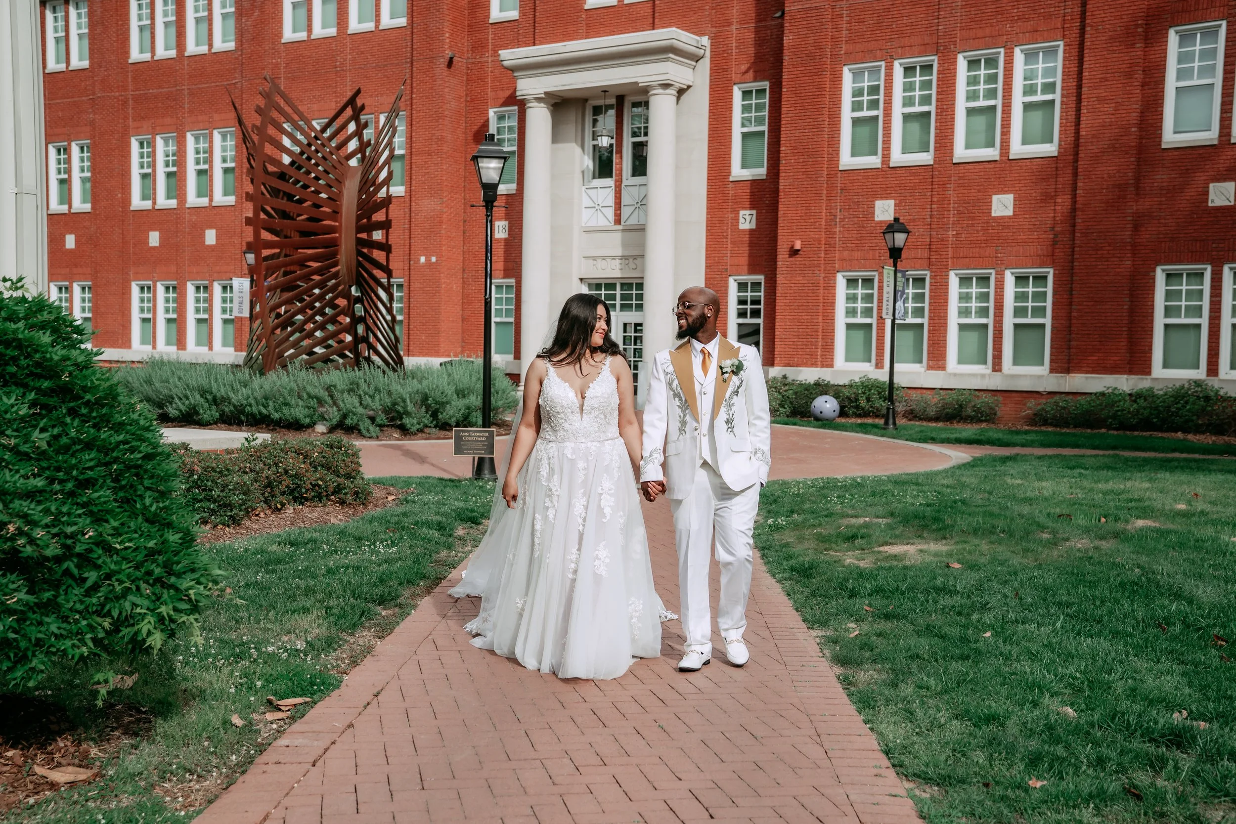 Bride and groom walk hand in hand along the brick paths at Queens University — planned by Charlotte Wedding Planner.