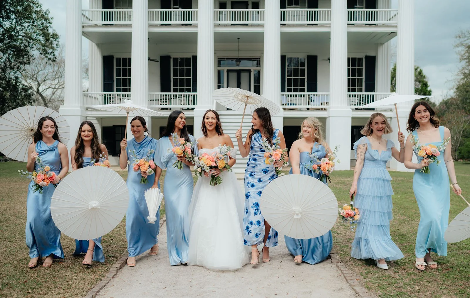 Bride walking with bridesmaids in blue dresses holding bouquets, showcasing ‘something blue’ wedding inspiration with cohesive color styling and elegant outdoor setting.