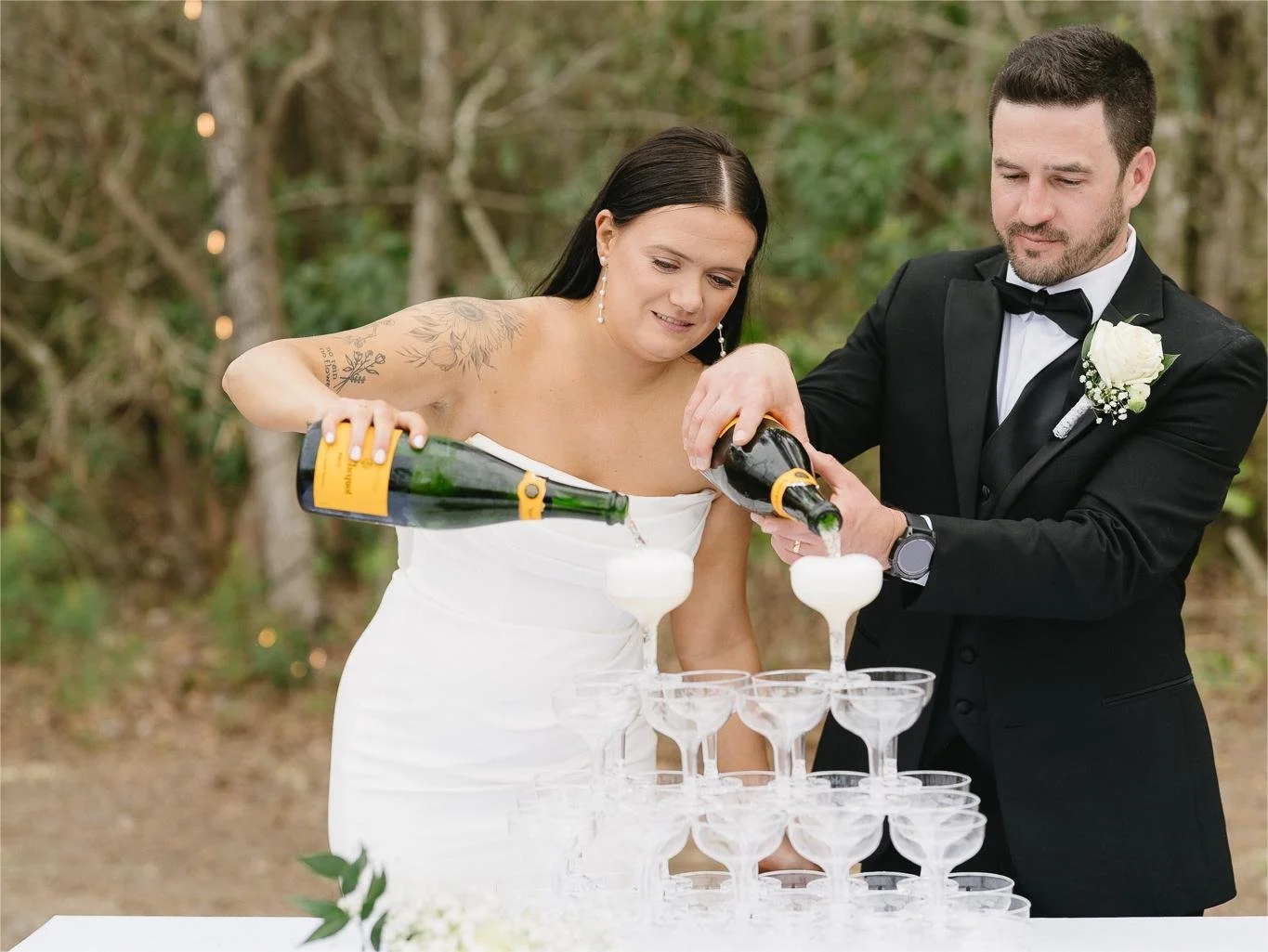 Bride and groom pouring champagne into a tower of glasses.