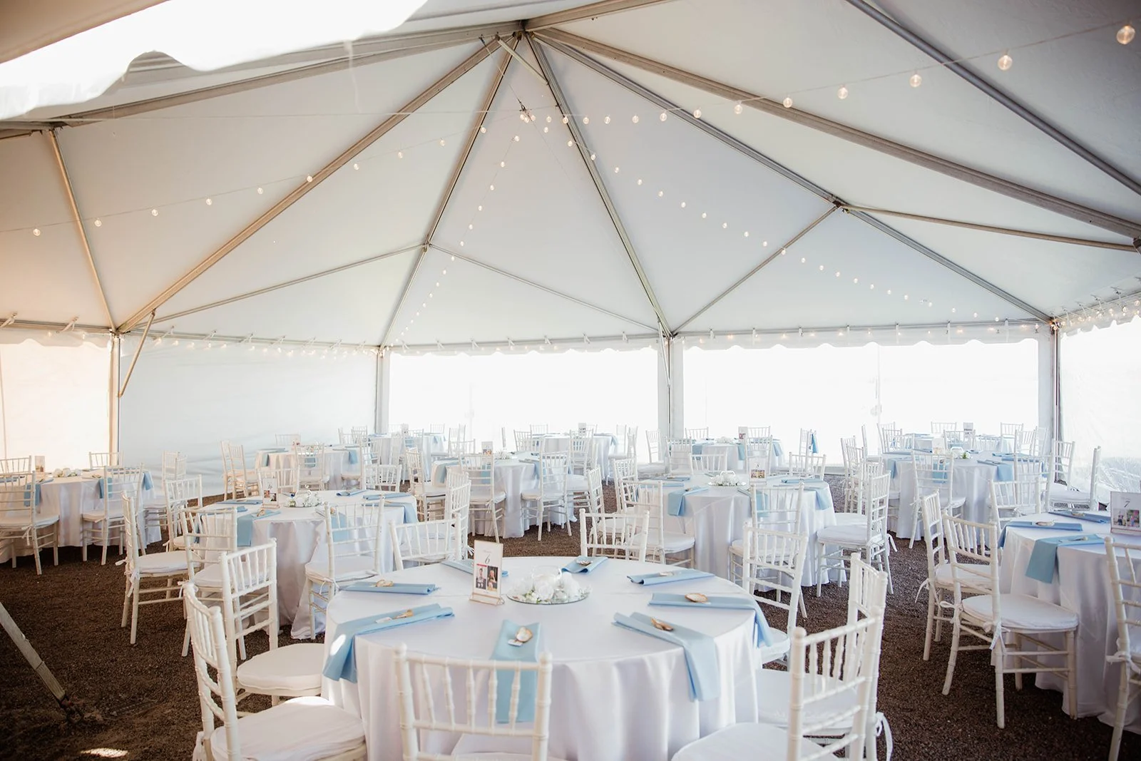 An outdoor tent setup with tables set for a reception, perfect for protecting guests from unexpected rain or sun exposure during a wedding celebration.