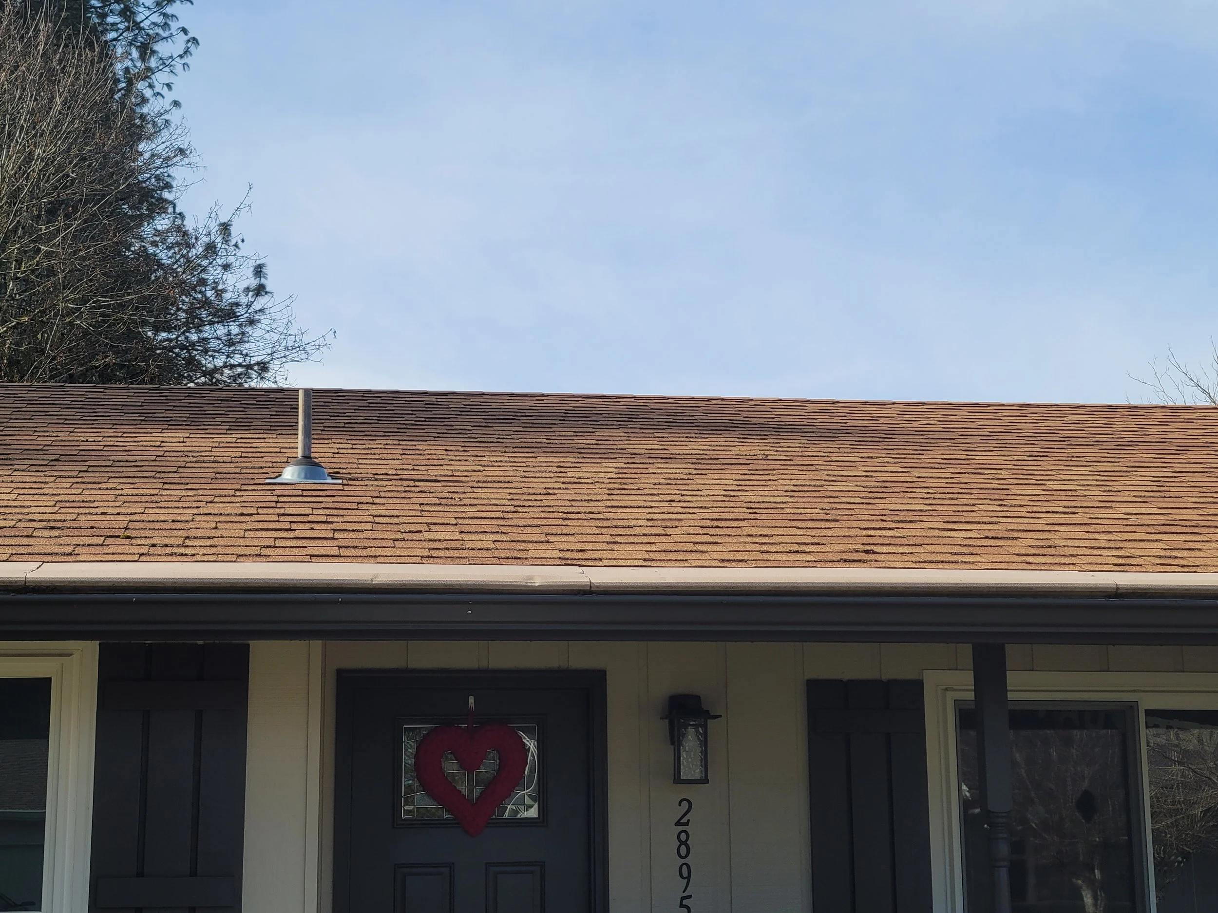 Front porch of a house with a red heart-shaped wreath on the black front door, house number 2895, and a sky with some clouds in the background.