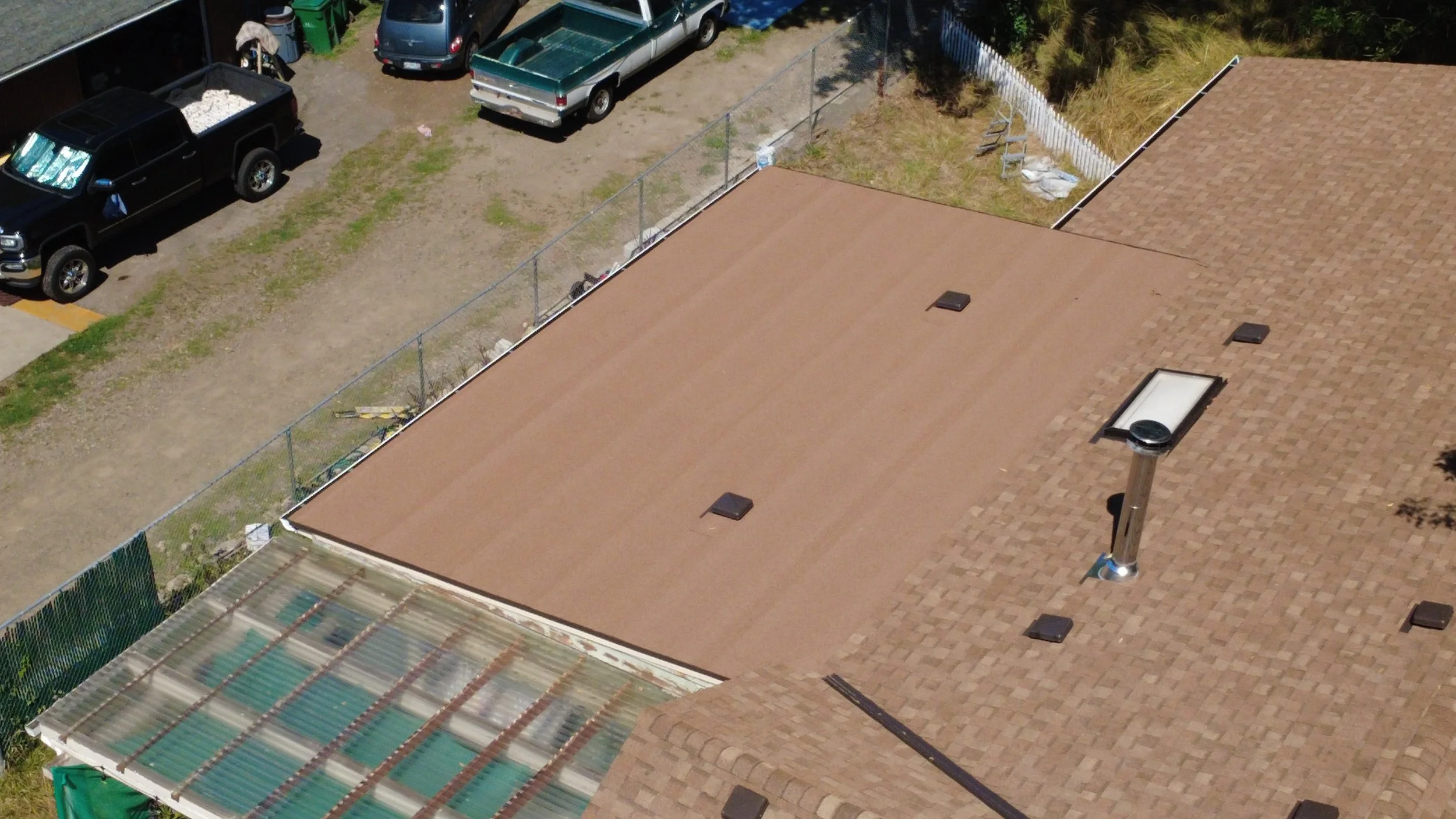 Aerial view of rooftops, parked cars, and a fenced area with construction materials.