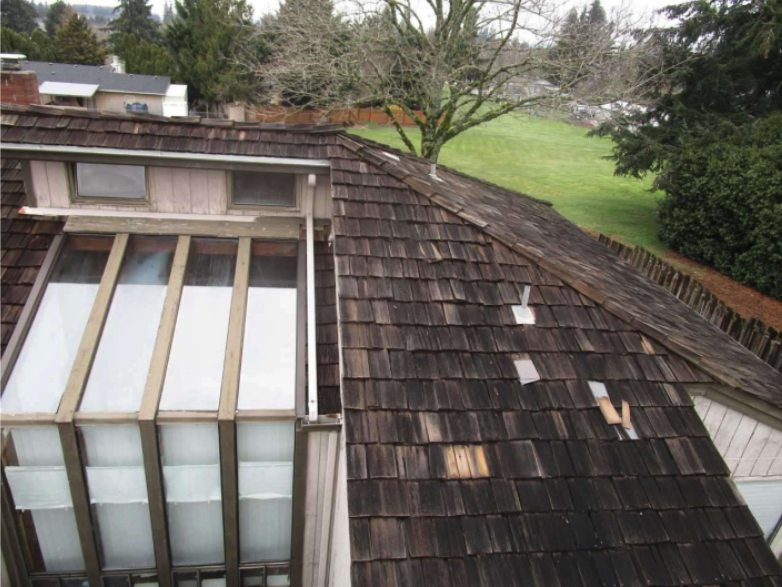 Aerial view of a house roof with old, weathered shingles, some tiles being replaced with new wood framing and a skylight.