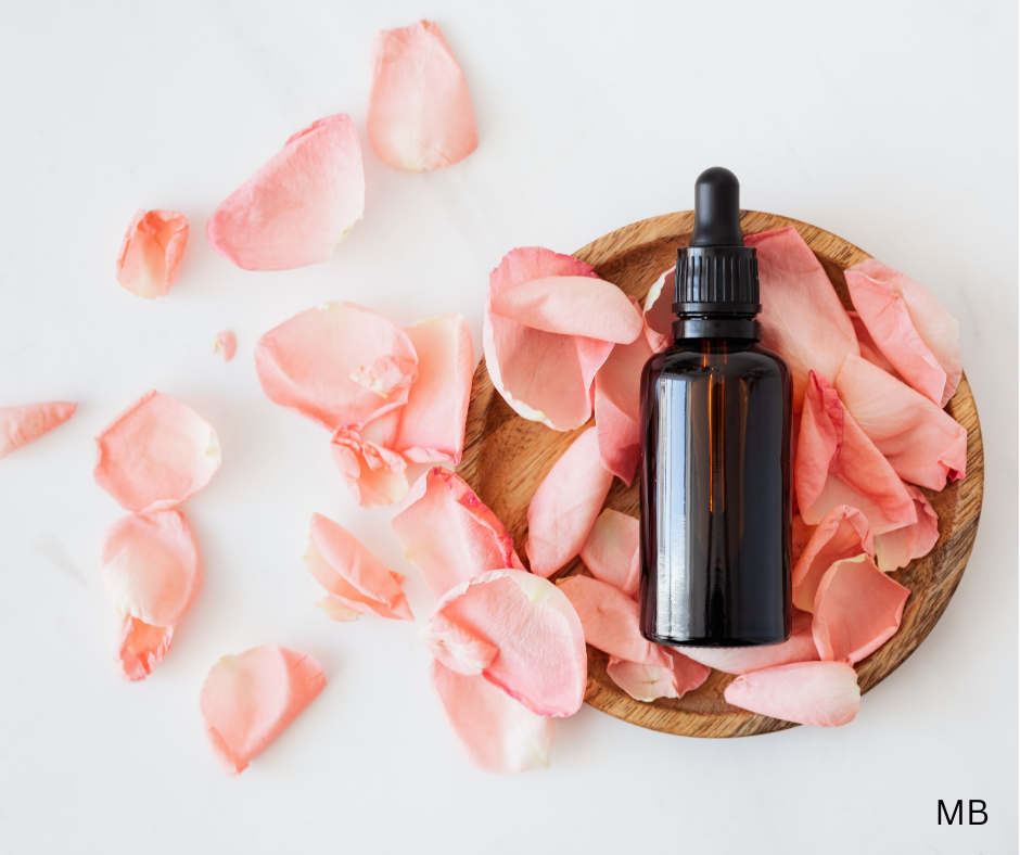 A brown dropper bottle on a wooden plate surrounded by pink rose petals.