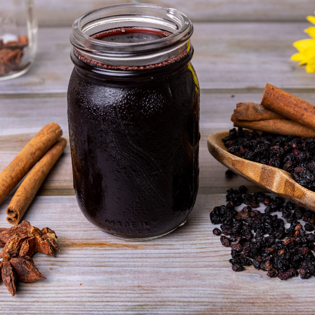 Homemade elderberry syrup in a glass mason jar surrounded by elderberries, cinnamon sticks, and star anise on a rustic wooden table.