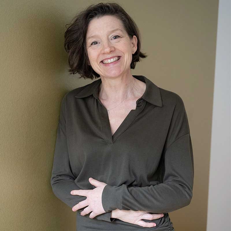 Porträt von Sandra Stark. Sie schaut freundlich, lachend direkt in die Kamera, trägt eine dunkelgrün/ braune Bluse, hat braune, kinnlange Haare.
