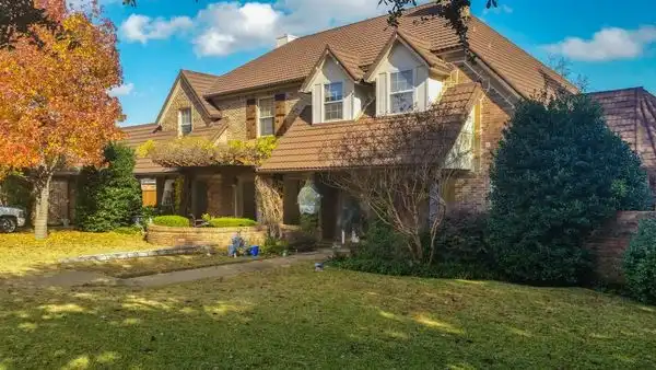 A large, two-story house with a brown roof and brick exterior, surrounded by a green lawn and trees with autumn foliage.