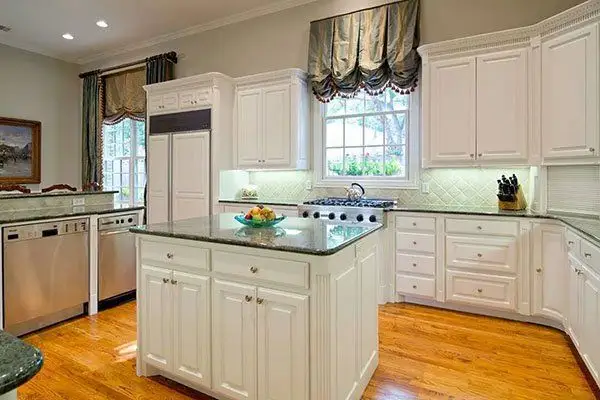Bright kitchen with white cabinets, green granite countertops, center island, wooden floor, and stainless steel appliances.