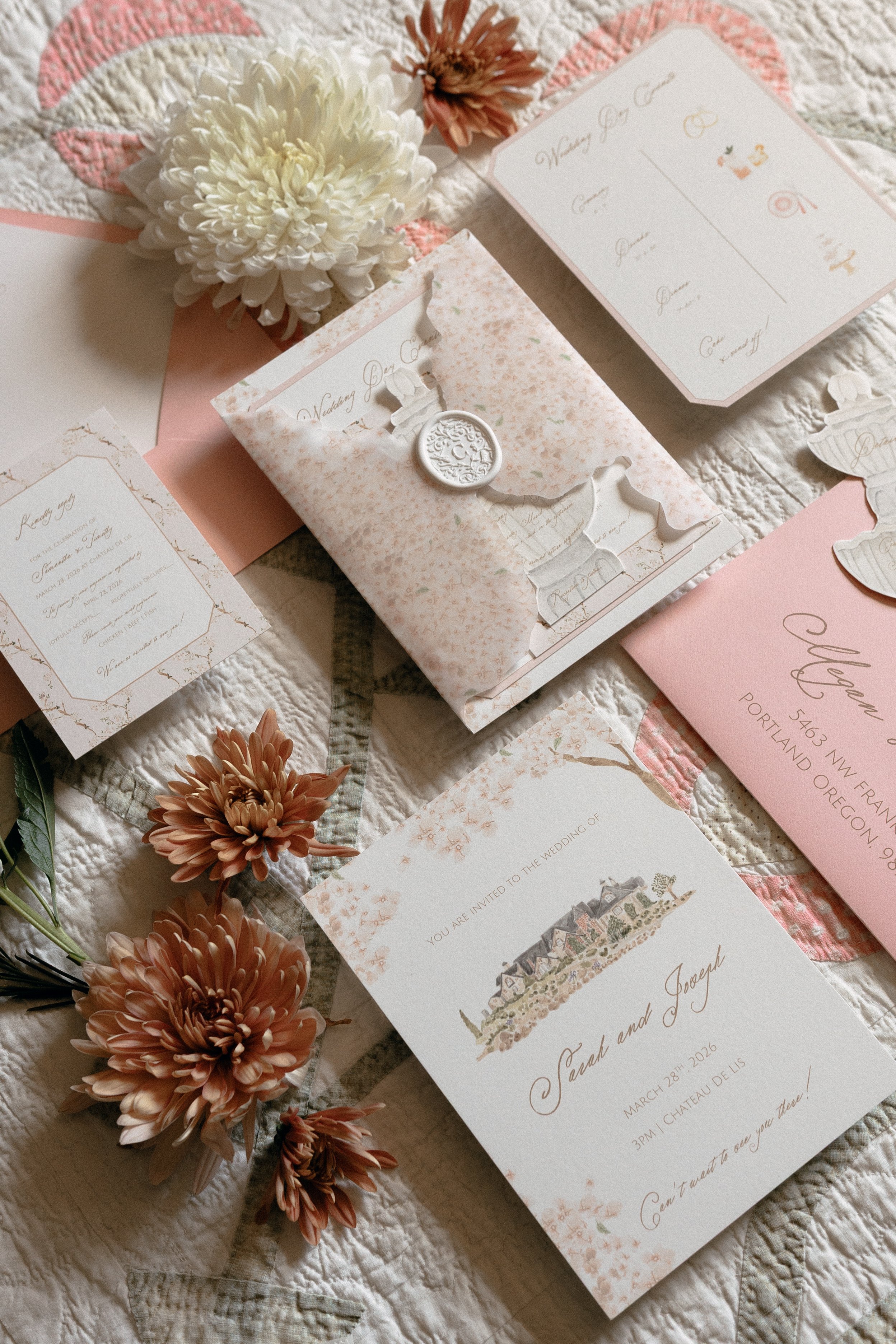 Wedding invitation cards, pink and white flowers, and pink paper on a quilted fabric background.