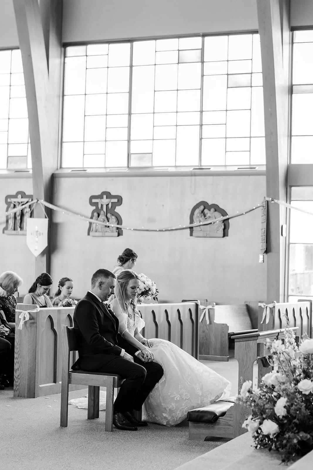 A wedding ceremony taking place inside a church, with the bride and groom sitting together at the altar, surrounded by guests.