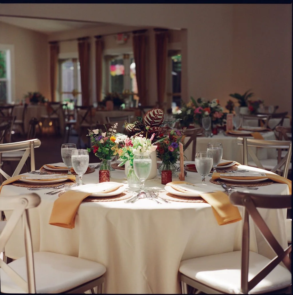 A banquet hall with a round table decorated with a floral centerpiece, water glasses, napkins, and tableware, set for a formal event.