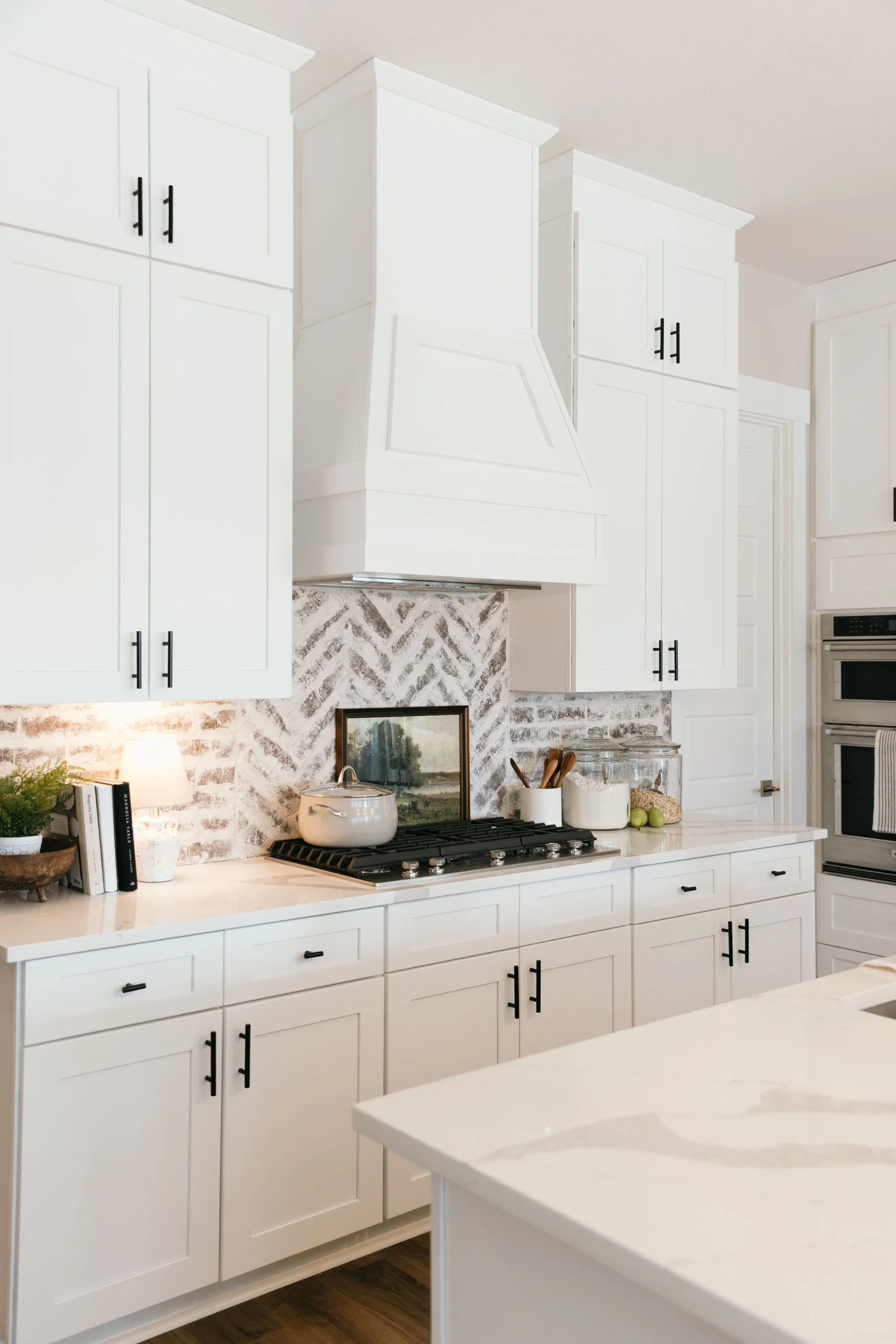 Modern white kitchen with black cabinet handles, a gas stove, and a decorative backsplash. Occupied and vacant staging Mckinney