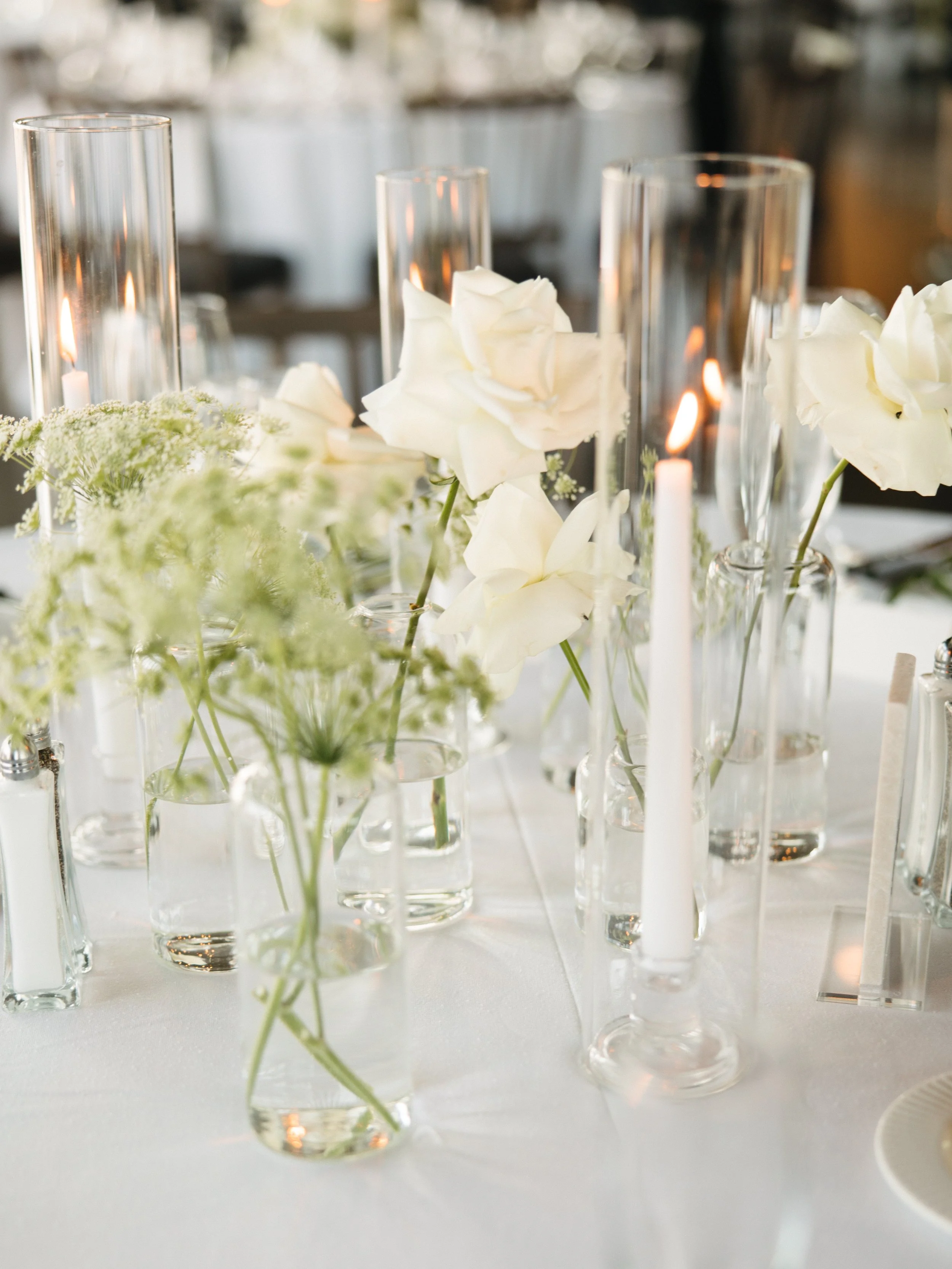 A table centerpiece with white flowers and tall glass candle holders with lit candles.